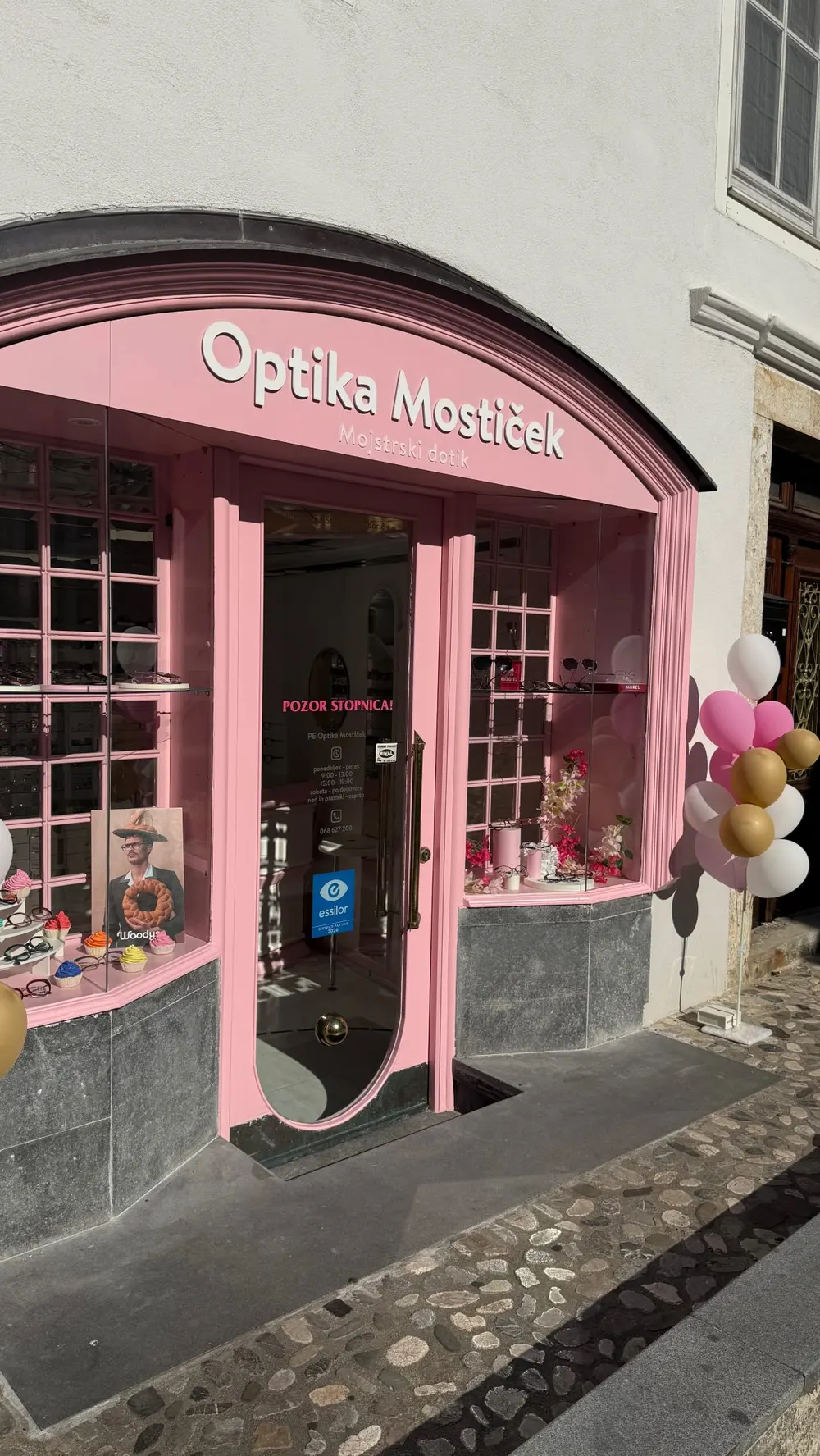 Rožnata izložba optike Mostiček v Kranju z napisom Mojstrski dotik
